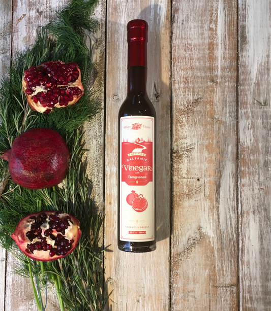 a bottle of Olive Crate pomegranate Balsamic vinegar next to fresh Pomegranate and herbs