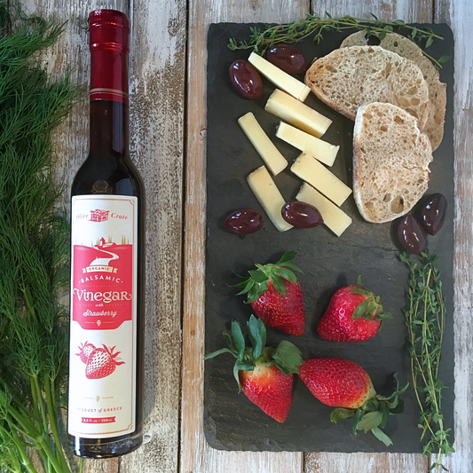 a bottle of Olive Crate strawberry Balsamic vinegar, cheese and strawberries on a cutting board