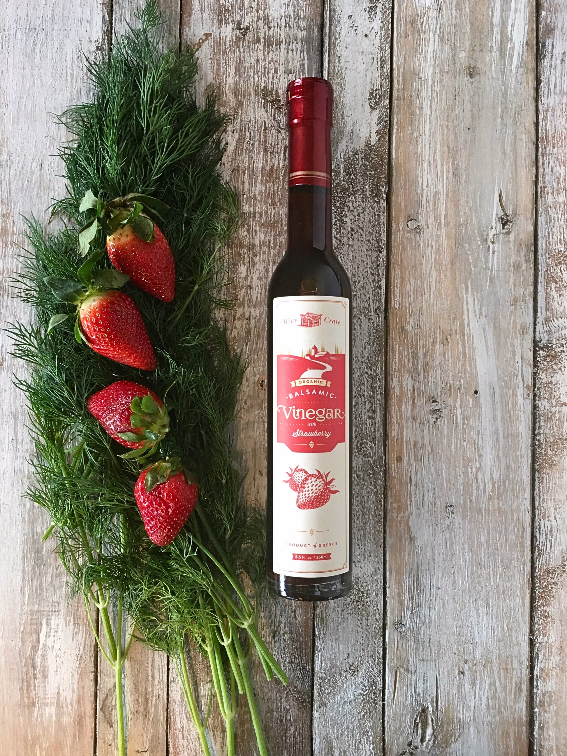 a bottle of Olive Crate organic strawberry balsamic vinegar next to strawberries and dill on a rustic board
