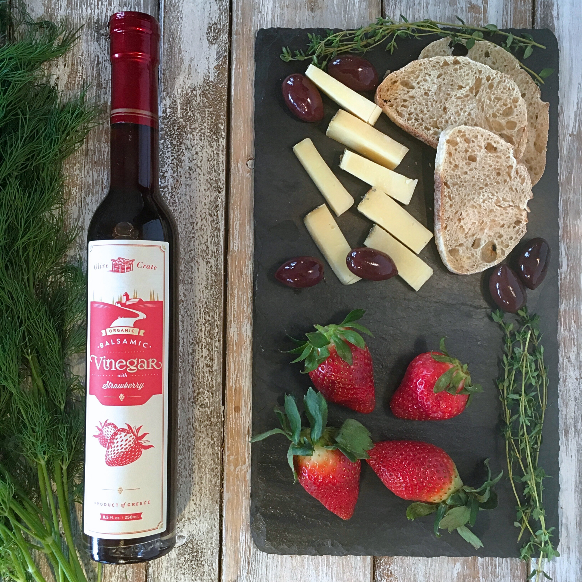 a bottle of Olive Crate strawberry Balsamic vinegar, cheese and strawberries on a cutting board