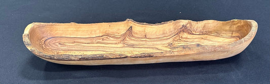 Hand-carved olive wood bread dish with natural bark edge and deep hollow, on dark blue background
