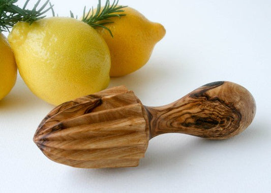Hand-carved olive wood citrus juicer, white background with lemons and herbs