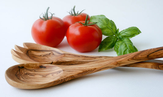Olive wood salad servers pair with raffia wrap at stem, fresh tomatoes and basil in background