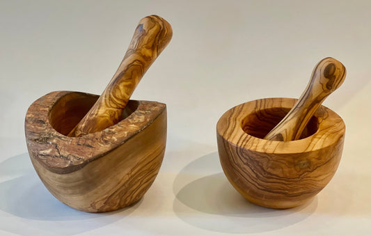 Two hand-carved olive wood mortar and pestle sets side by side. The larger 5.5 inch natural edge and the smaller 4.5 inch smooth edge finish.