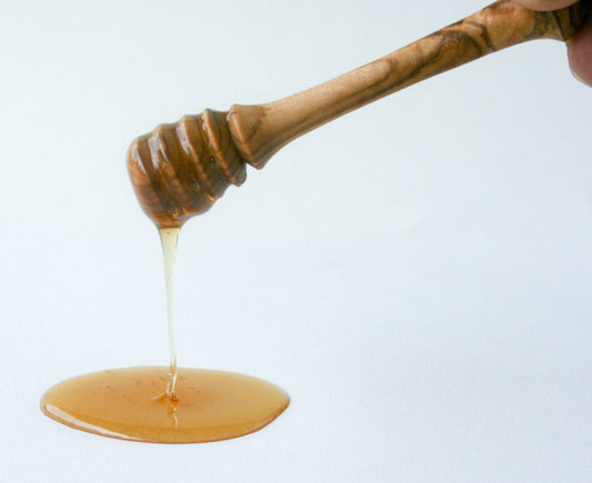 Hand-carved olive wood honey dipper with honey dripping off spiral grooves, white background